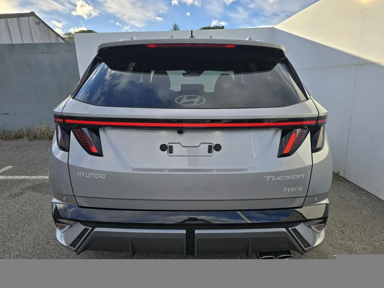 Vue arrière d'un Hyundai Tucson hybride 2025 en argent métallisé avec feux arrière LED et double sortie d'échappement.