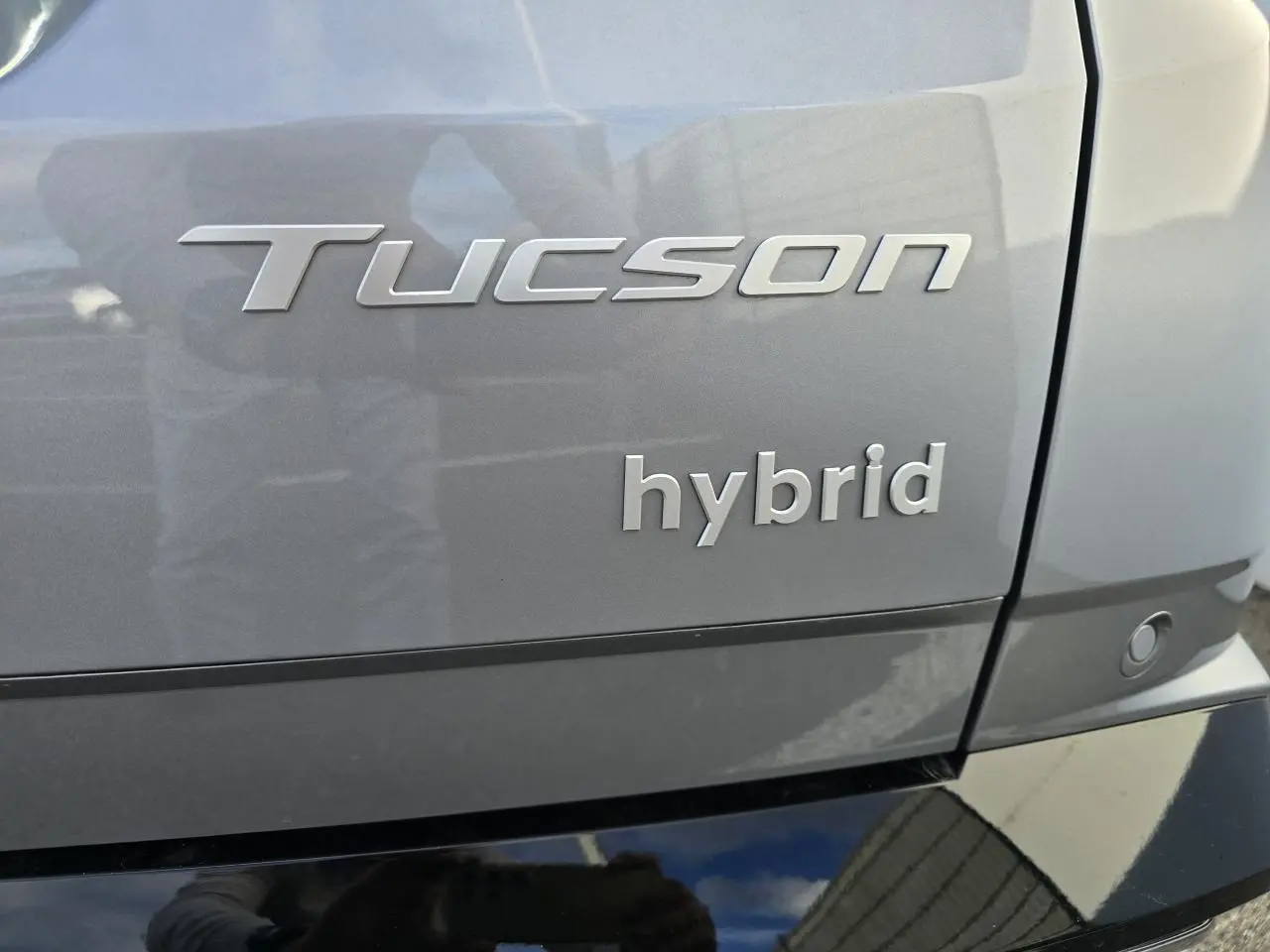 Gros plan sur l’arrière droit d’un Hyundai Tucson 2025 hybride en gris métallisé avec badges Tucson et hybrid visibles.