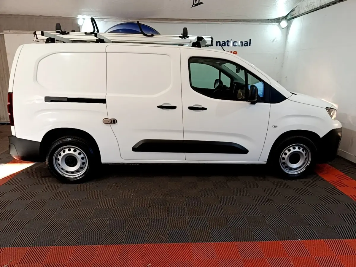 Vue latérale droite d'un utilitaire Peugeot Partner blanc avec galerie de toit et jantes acier en intérieur fermé.