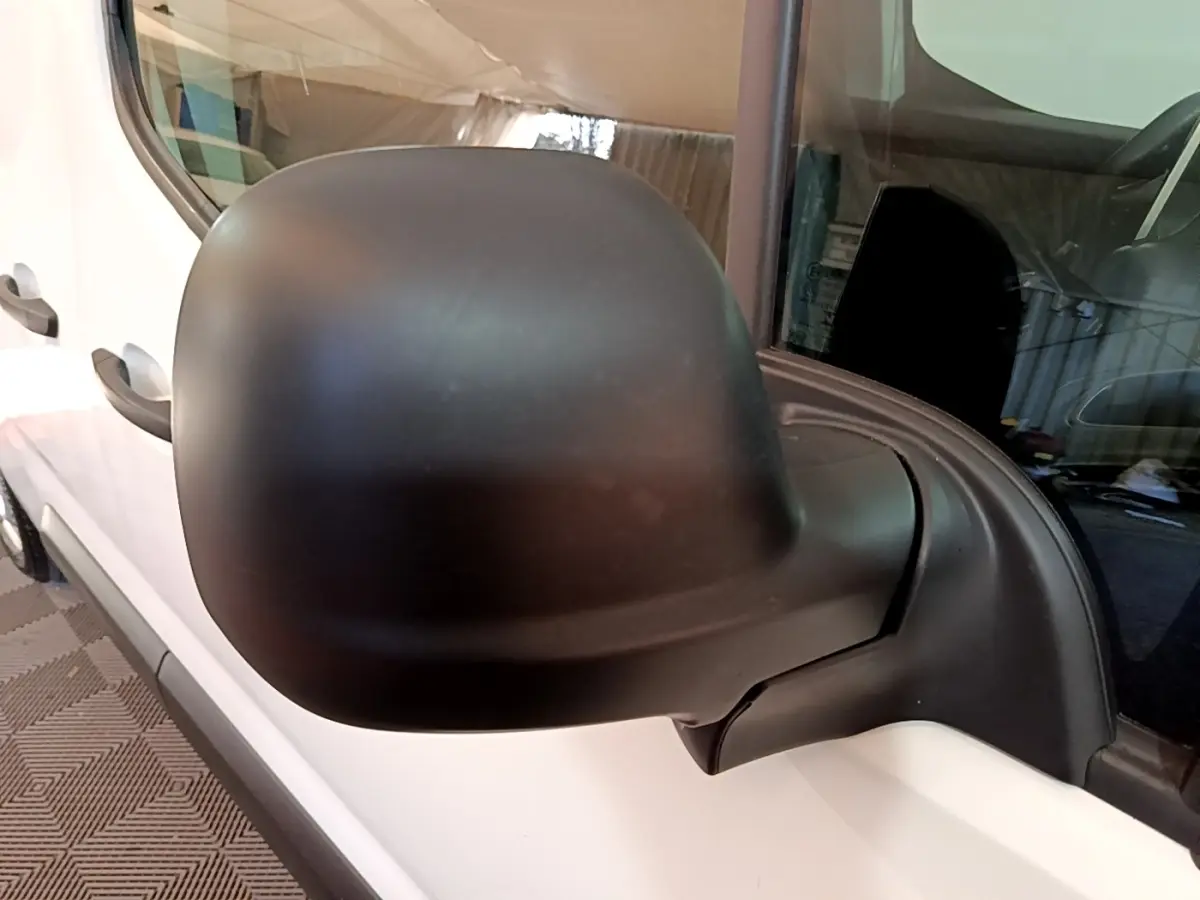 Rétroviseur noir en gros plan côté gauche d’un Peugeot Partner blanc, vue partielle du véhicule côté conducteur.