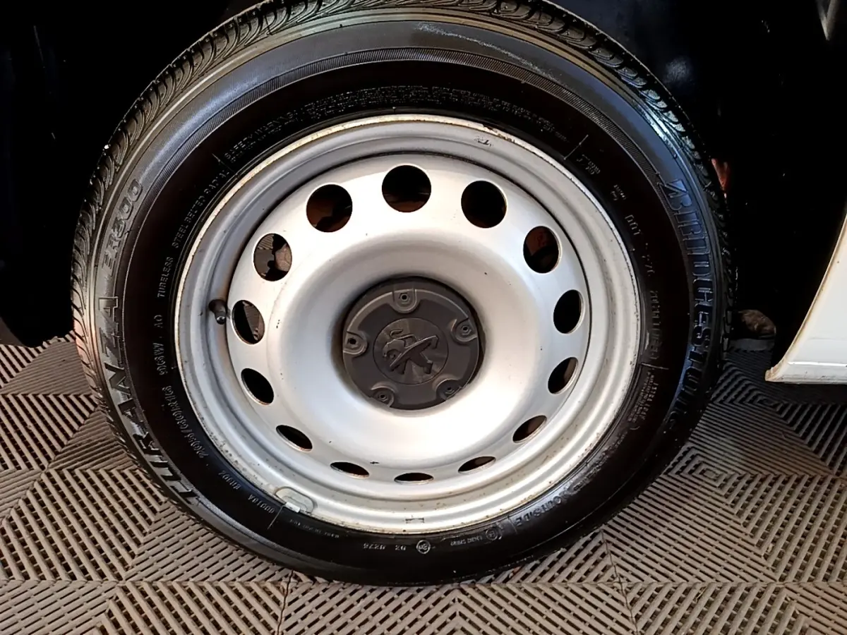 Gros plan sur la roue acier blanche avec logo Peugeot d’un Peugeot Partner blanc, vue côté droit.