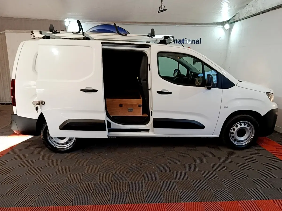 Vue de profil côté droit d’un Peugeot Partner blanc avec porte coulissante ouverte et chargement visible.