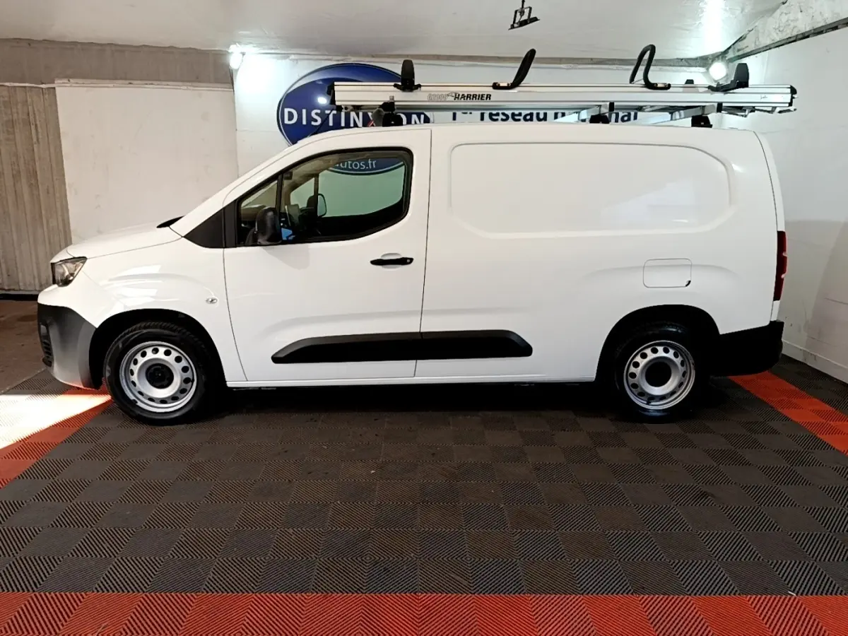 Vue latérale gauche d’un utilitaire Peugeot Partner blanc avec galerie de toit et jantes acier en intérieur fermé.