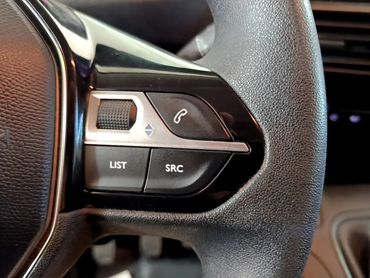 Gros plan sur les commandes gauche du volant noir du Peugeot Partner blanc, boutons LIST, SRC et téléphone visible.