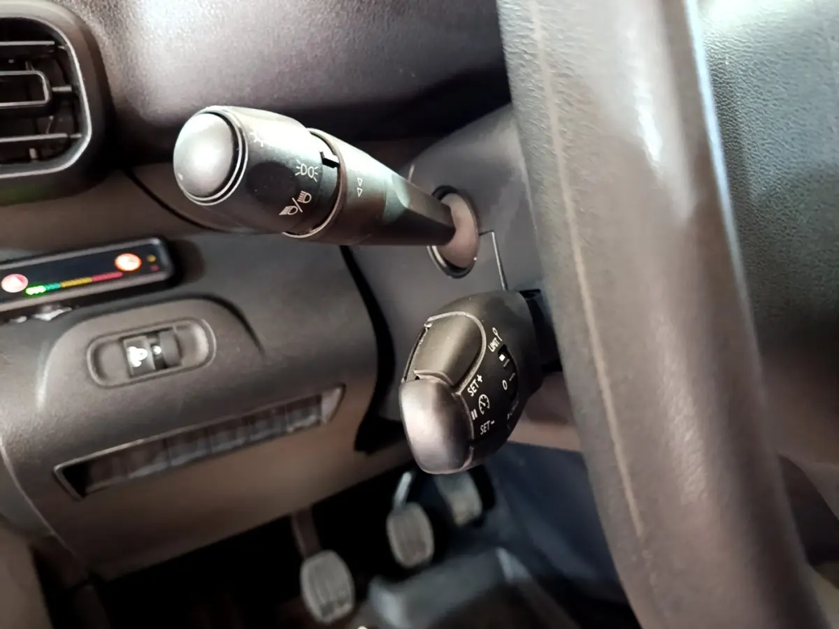 Gros plan sur les commandes au volant noir du Peugeot Partner blanc, avec levier de clignotants et régulateur de vitesse.