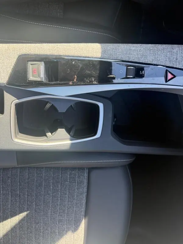 Vue plongeante sur la console centrale grise du Peugeot 3008 Hybrid 145 Allure, avec porte-gobelets et commandes de frein à main électrique.