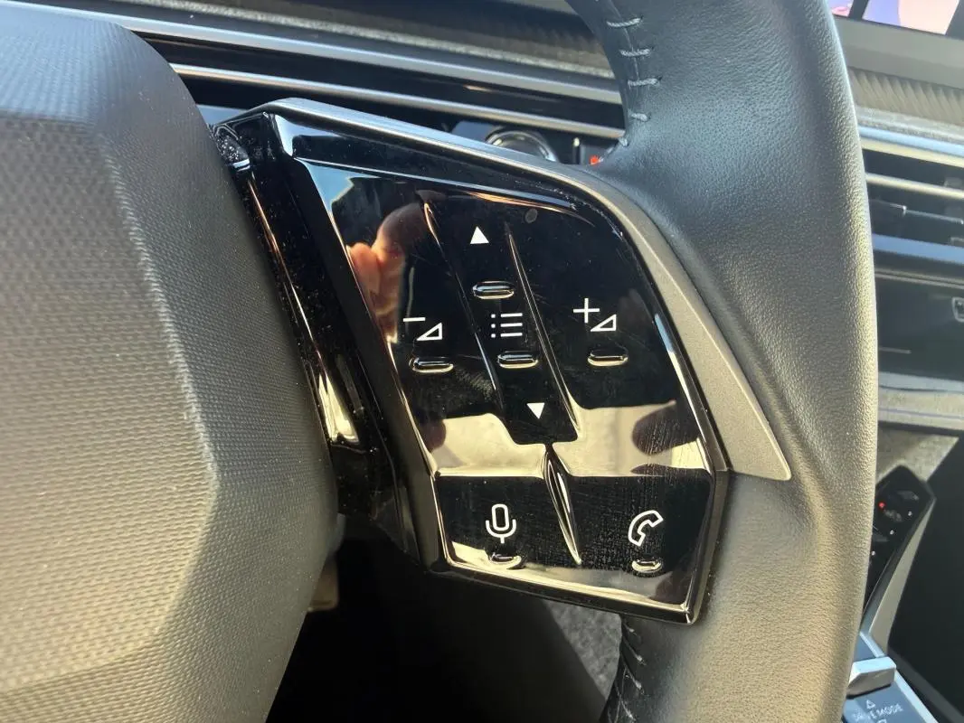 Gros plan sur les commandes tactiles noires à gauche du volant du Peugeot 3008 Hybrid gris, avec micro et téléphone.