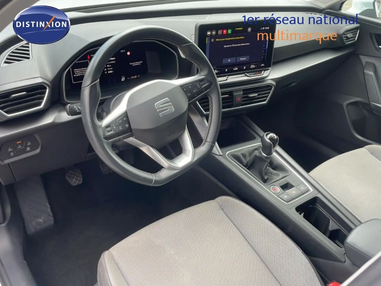Vue intérieure de face du poste de conduite du SEAT LEON blanc neige métal, avec volant cuir multifonction et boîte manuelle.