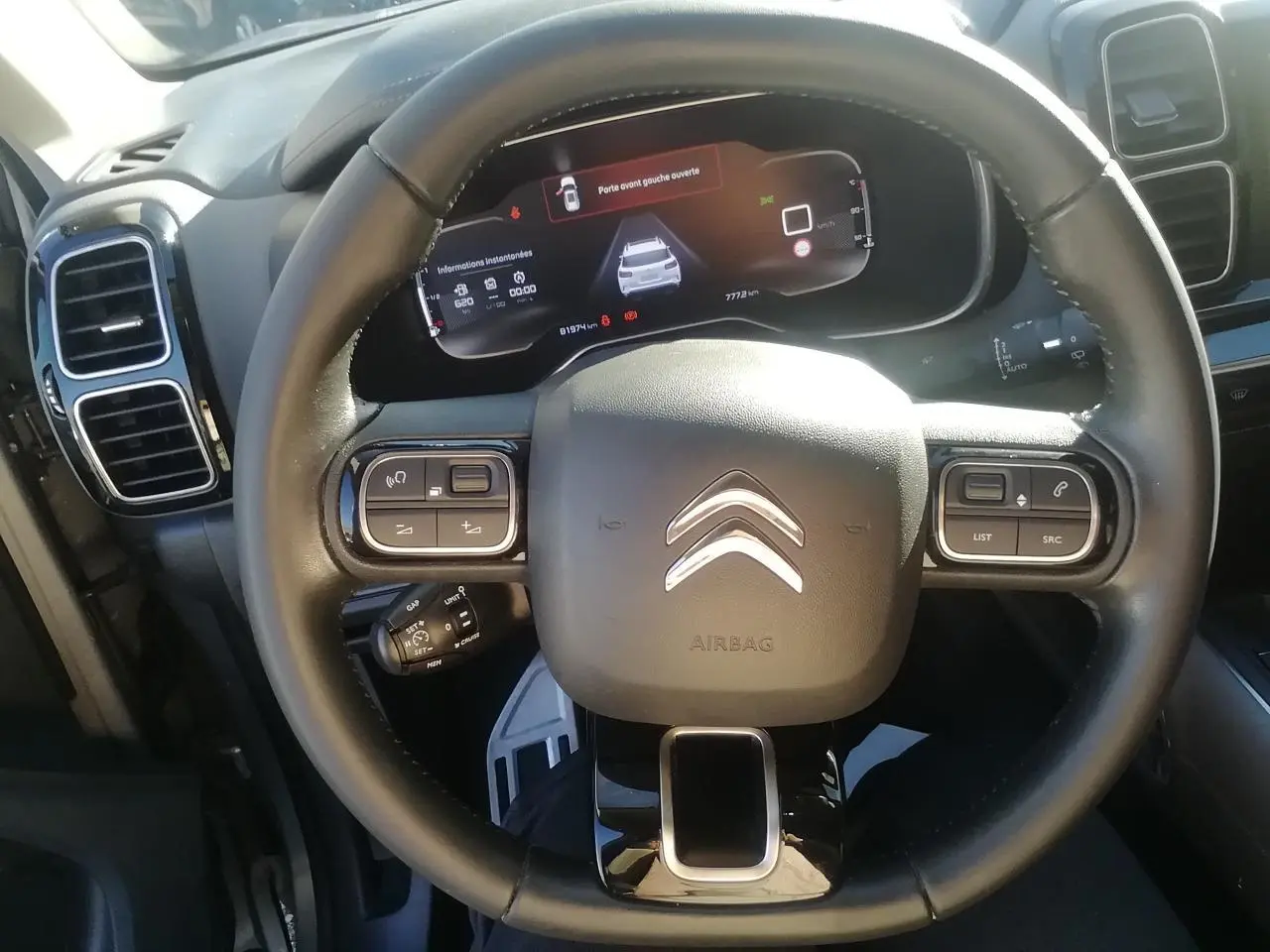 Vue rapprochée du volant noir du Citroën C5 Aircross avec tableau de bord numérique affichant une porte ouverte.