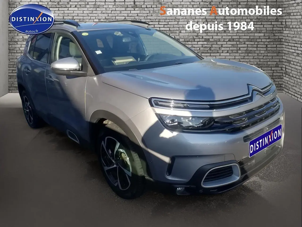 Vue 3/4 avant d'un Citroën C5 Aircross gris métallisé avec jantes alliage et barres de toit bi-ton.
