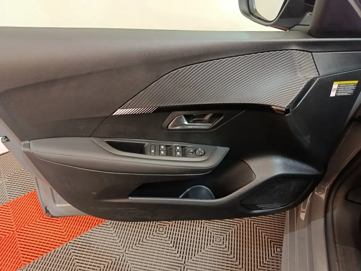 Vue côté gauche de la porte avant gris foncé du Peugeot 208 PureTech 100 S&S Allure avec commandes des vitres et décor carbone.