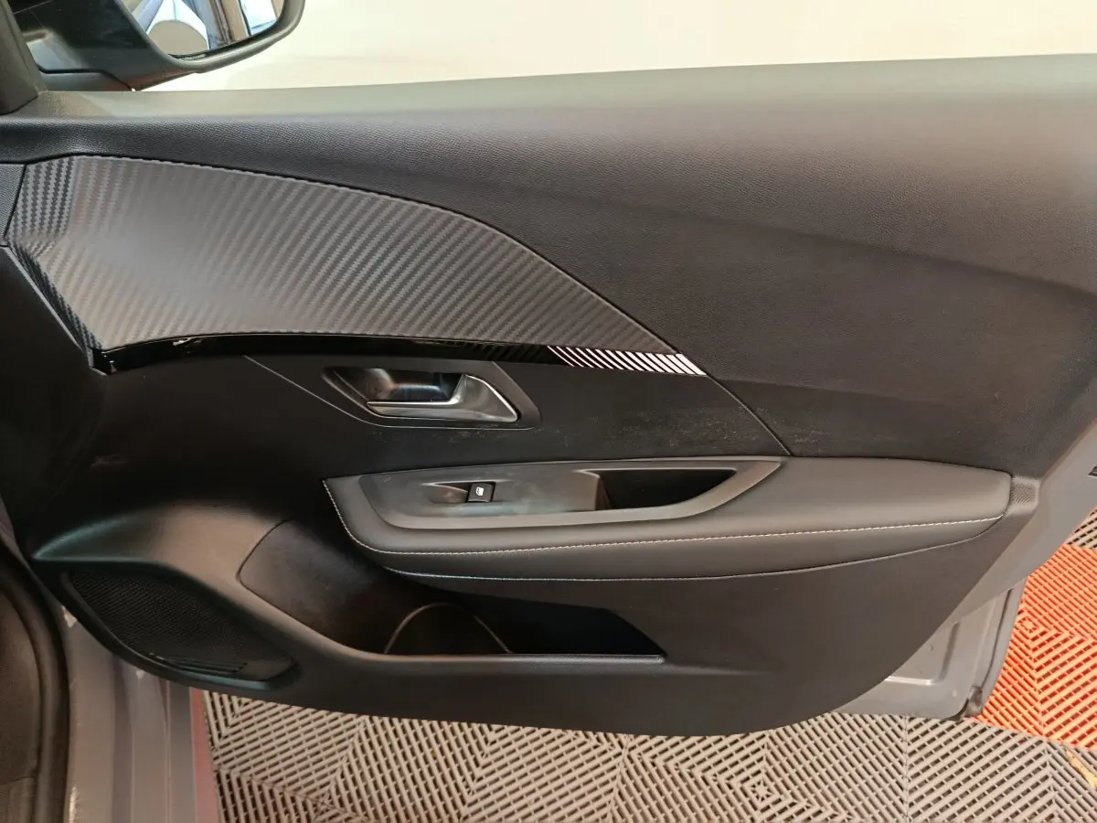 Gros plan sur la porte intérieure côté gauche de la Peugeot 208 gris foncé avec insert effet carbone et poignée métallique.