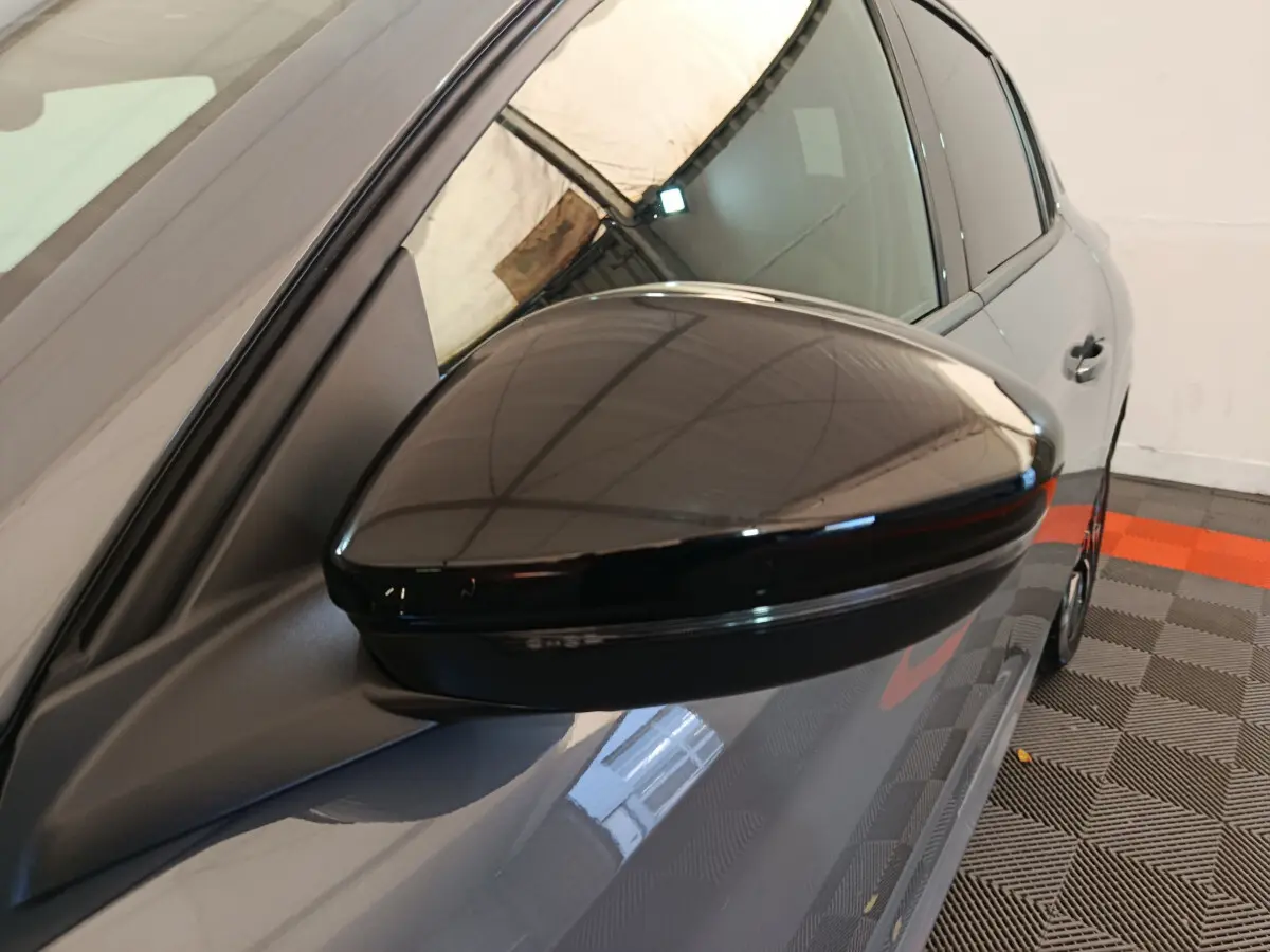 Rétroviseur noir brillant côté gauche d'une Peugeot 208 gris foncé vue en léger contre-plongée intérieure.