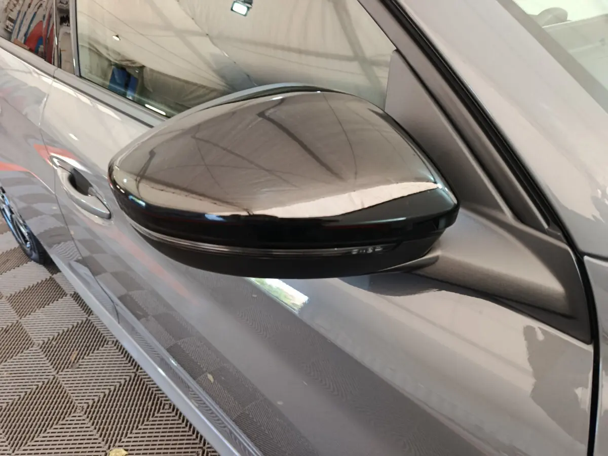 Rétroviseur noir côté gauche d'une Peugeot 208 gris foncé, vue rapprochée sur la portière avant.
