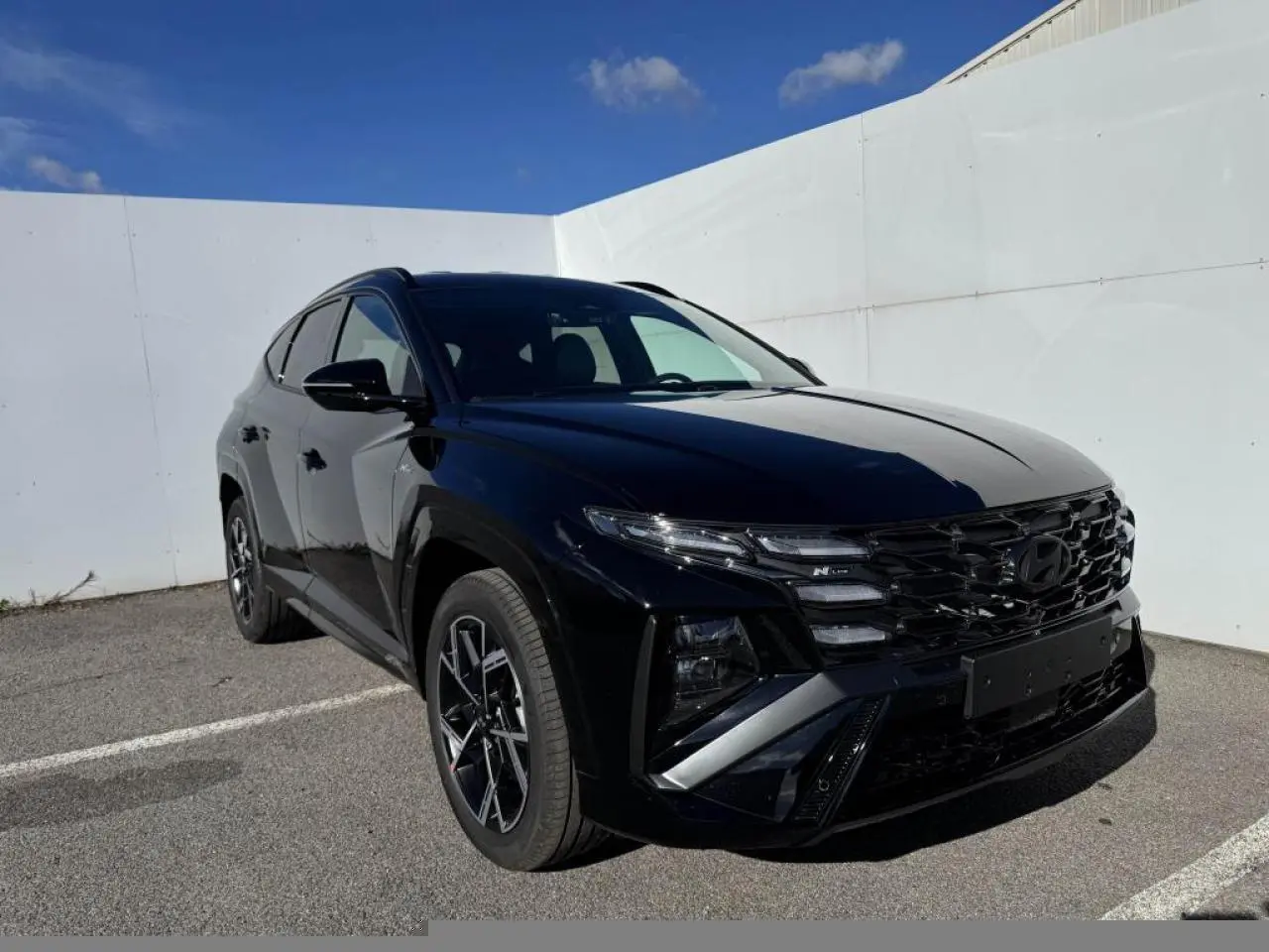 Hyundai Tucson IV noir abyss métal en 3/4 avant droit, avec calandre N Line et jantes alliage 19 pouces.