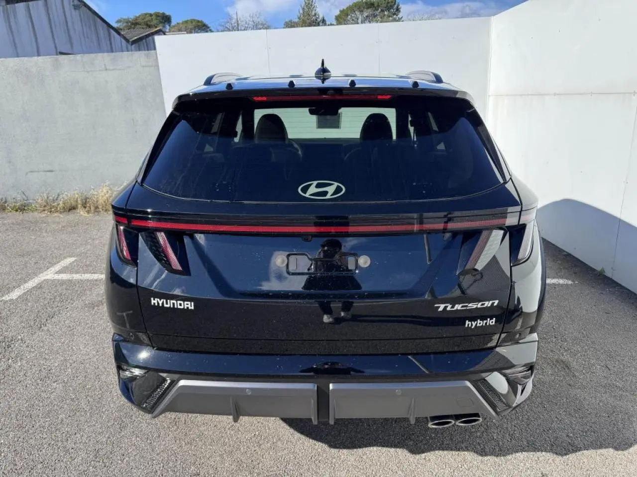 Vue arrière d'un Hyundai Tucson noir Abyss Metal avec feux LED reliés par un bandeau lumineux rouge.