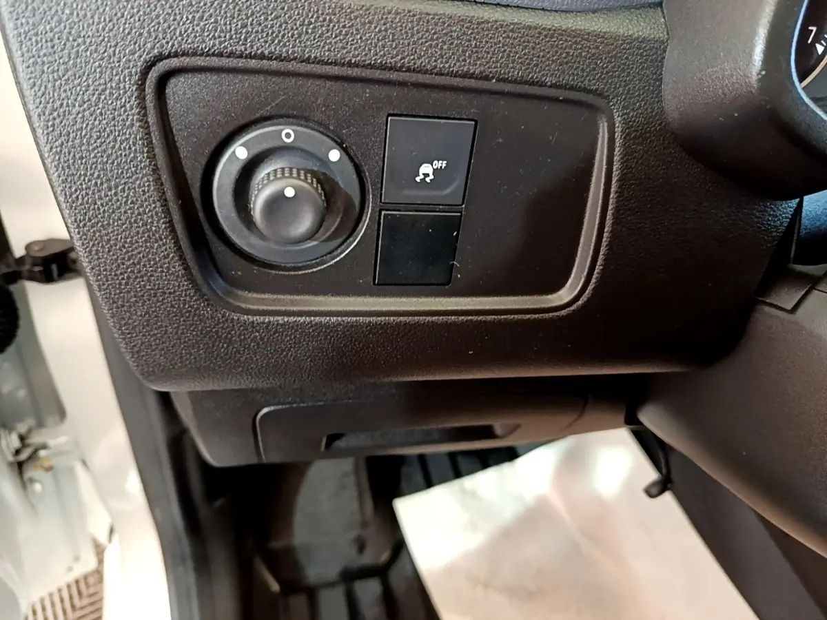 Gros plan sur les commandes de réglage des phares et antipatinage à gauche du volant d’un Renault Express blanc.