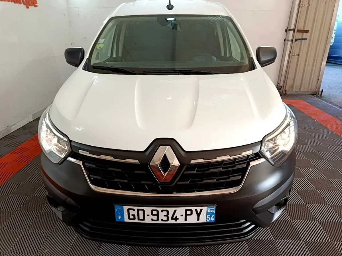 Vue avant d’un Renault Express blanc avec calandre noire et phares allumés dans un garage.