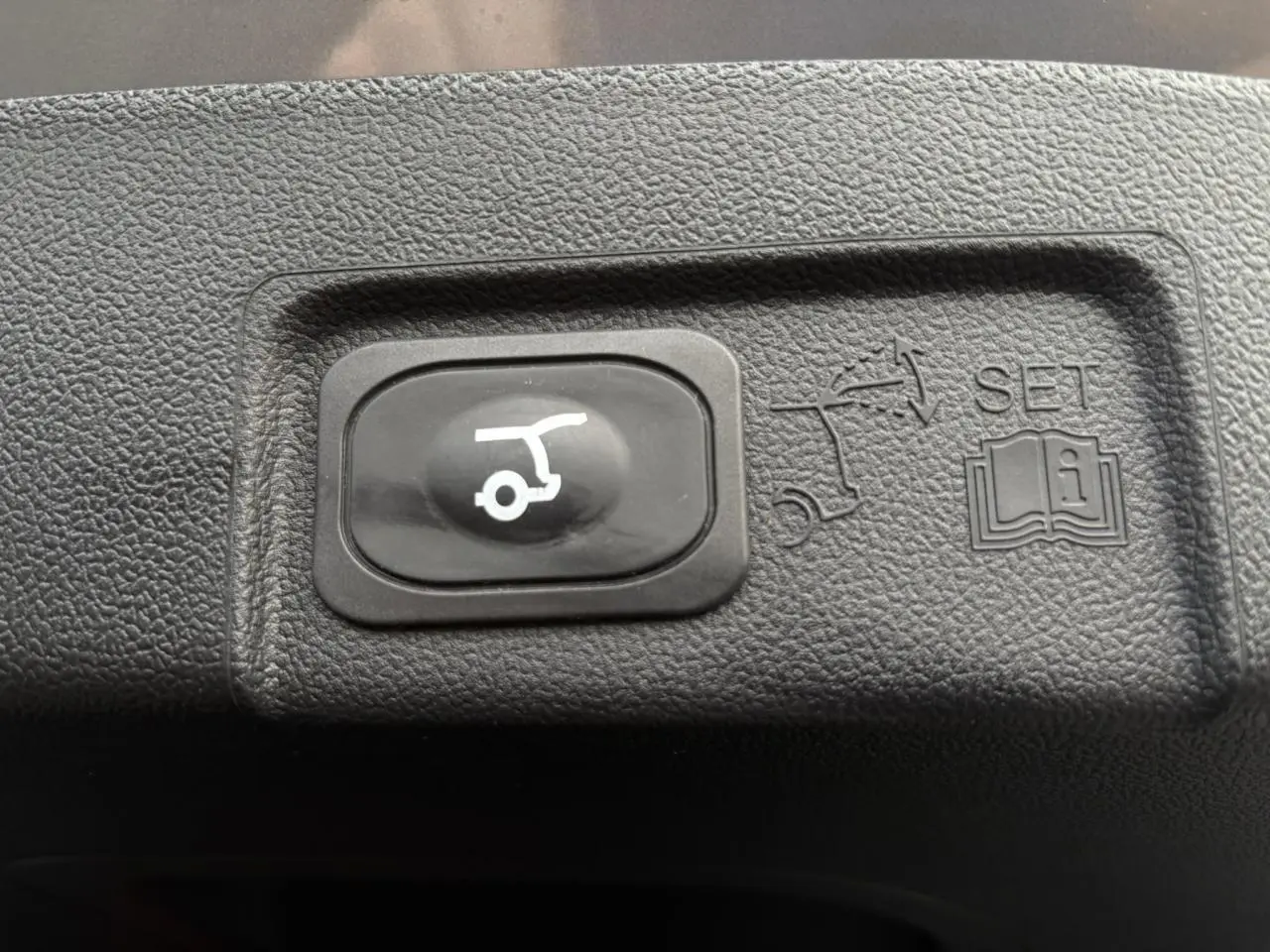 Bouton noir de hayon électrique avec pictogramme blanc sur plastique texturé intérieur d'un Ford Puma gris Solar 2023.
