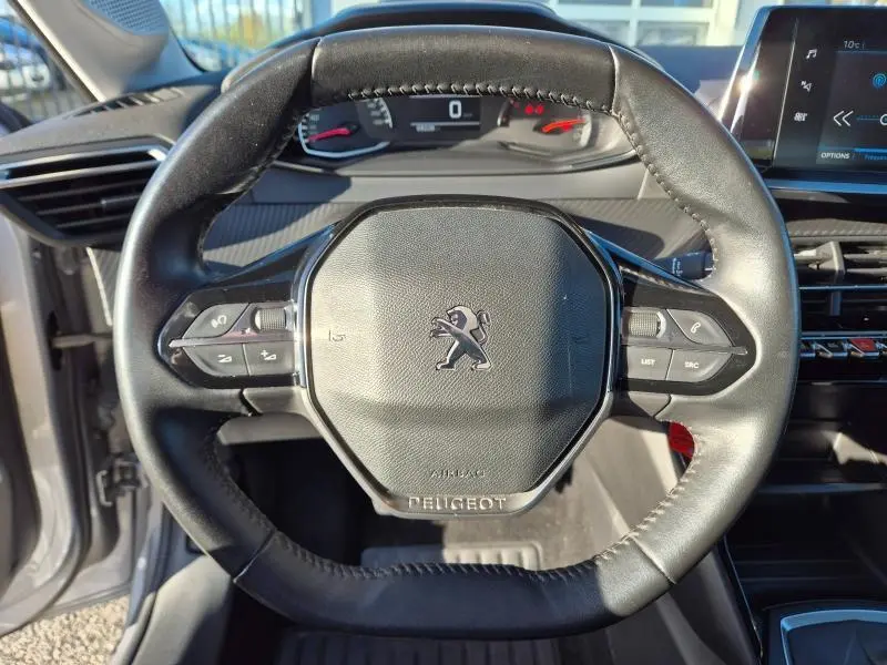 Vue rapprochée du volant cuir noir de la Peugeot 208 1.5 BlueHDi 2020 avec commandes intégrées et tableau de bord numérique.