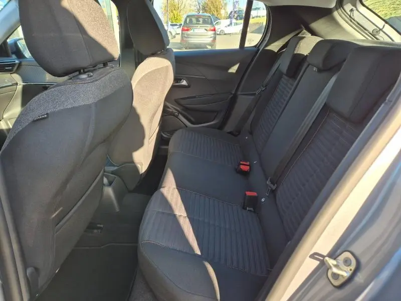 Vue intérieure arrière côté droit de la Peugeot 208 1.5 BlueHDi gris Artense, montrant la banquette et les sièges en tissu noir.