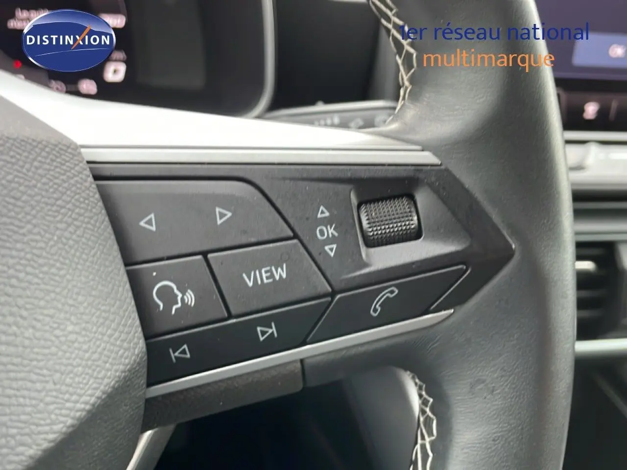 Gros plan sur les commandes gauche du volant en cuir noir du SEAT Leon bleu Fjord, avec boutons multifonctions visibles.