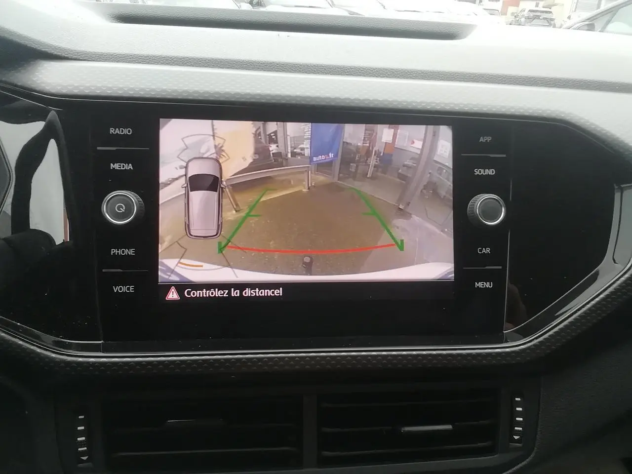 Écran tactile intérieur montrant la caméra de recul du Volkswagen T-Cross blanc, avec repères de guidage colorés.