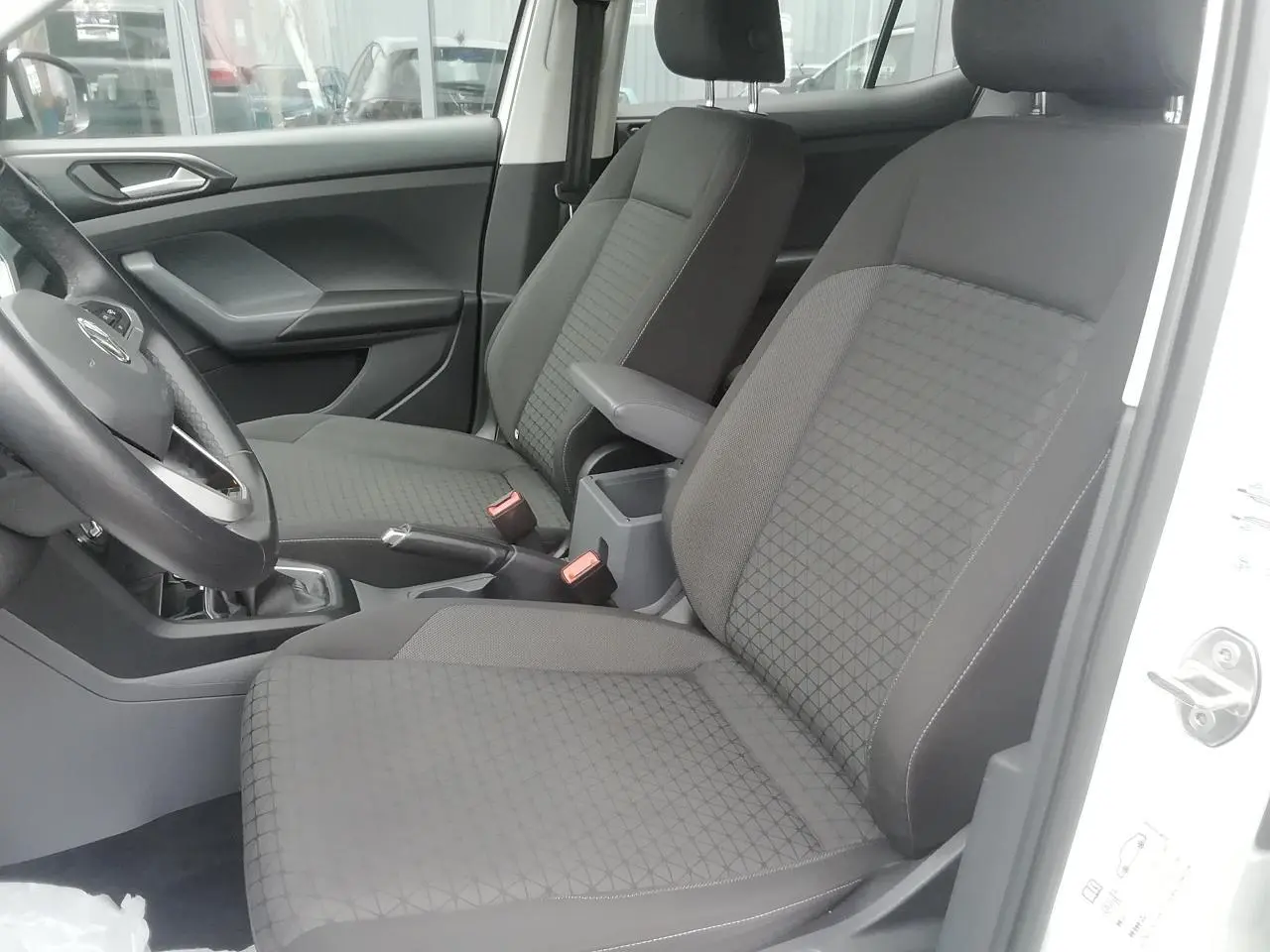 Vue intérieure côté gauche du Volkswagen T-Cross blanc 2020, montrant les sièges avant en tissu gris et l'accoudoir central.