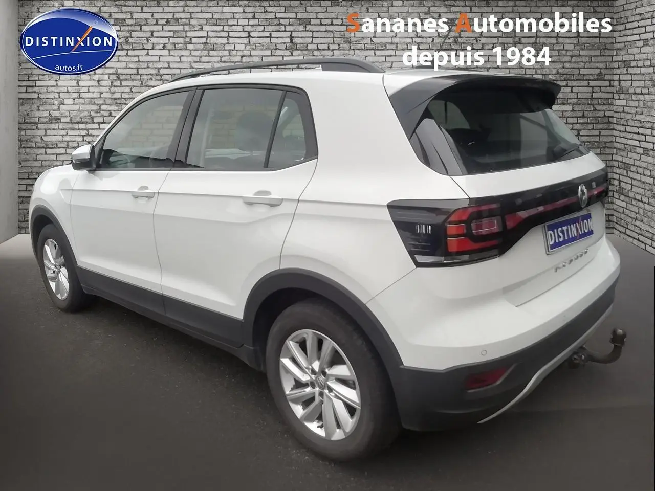 Vue 3/4 arrière droite d’un Volkswagen T-Cross blanc 2020 avec barres de toit noires et attelage.