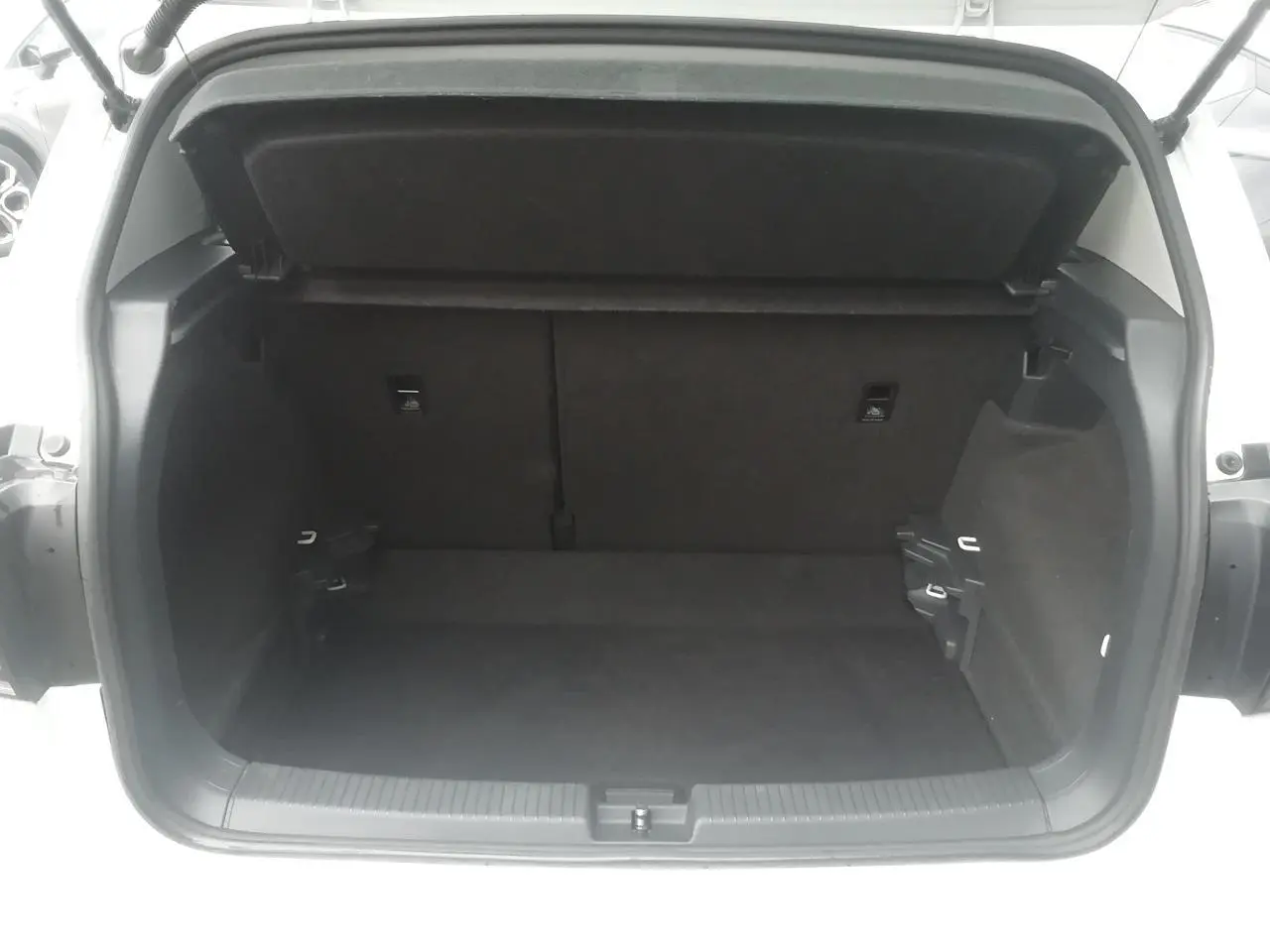 Coffre ouvert vu de l'arrière d'un Volkswagen T-Cross blanc, montrant l'espace de chargement vide et la garniture intérieure noire.