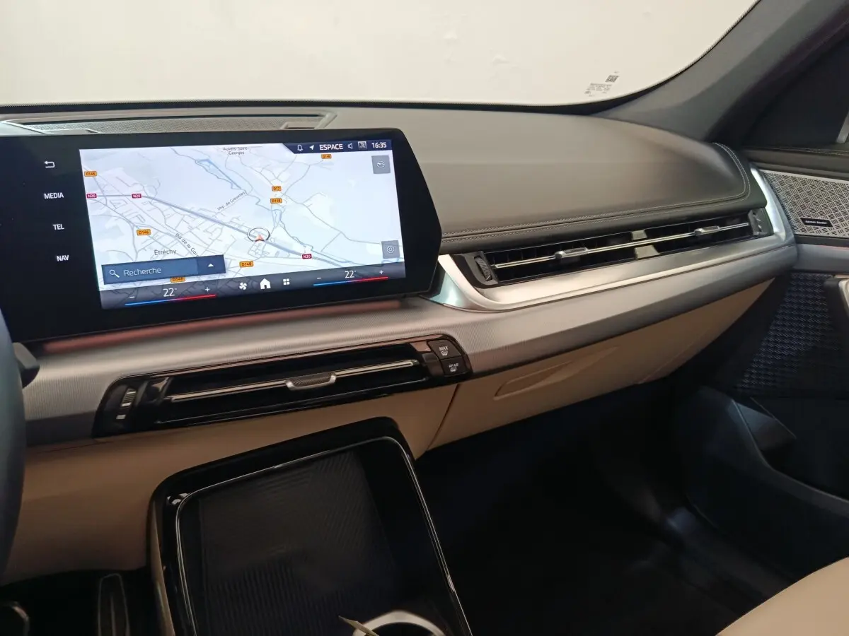 Tableau de bord beige et noir de BMW X1 xDrive25e M Sport 2024 avec écran tactile central affichant une carte.