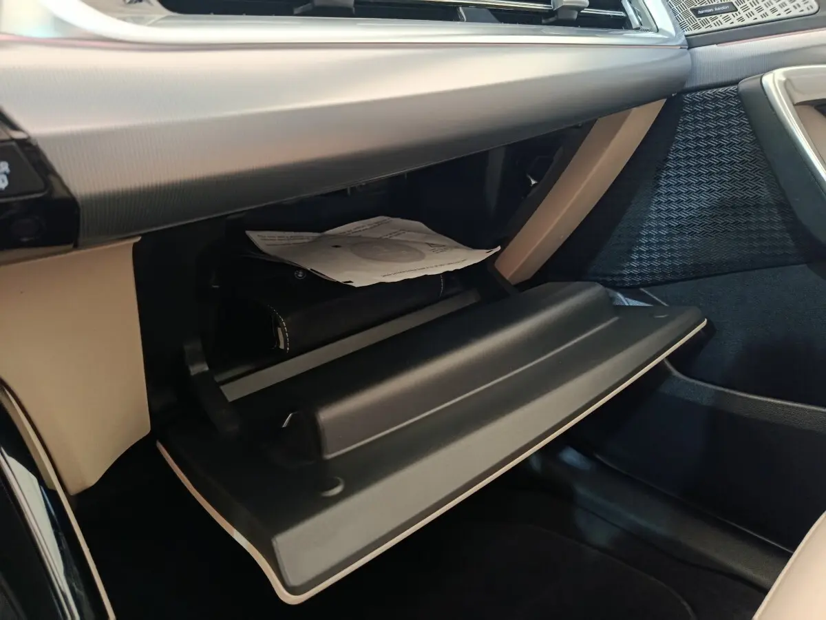 Gros plan sur la boîte à gants ouverte de la BMW X1 xDrive25e M Sport 2024, intérieur beige et noir.