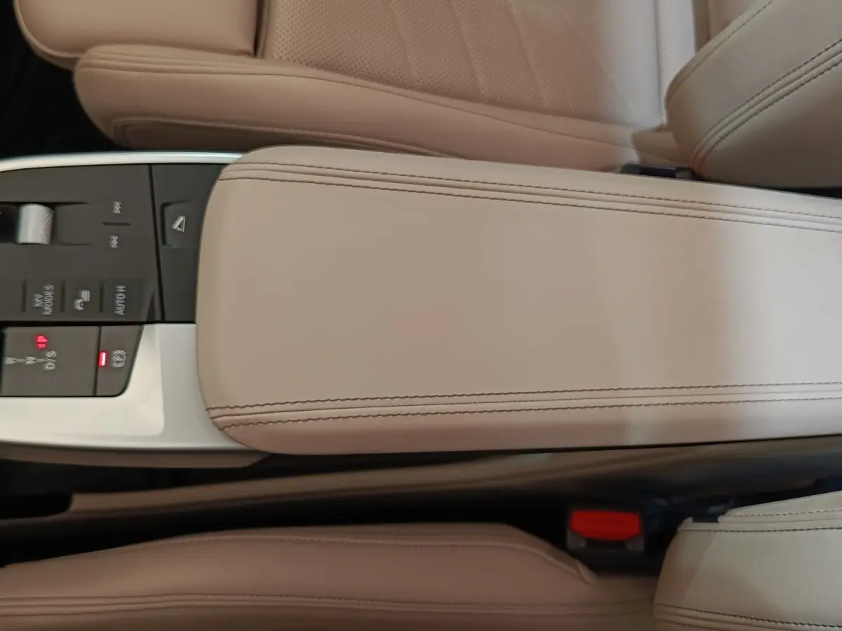 Gros plan sur l'accoudoir central beige et la console de commandes du BMW X1 xDrive25e M Sport 2024.