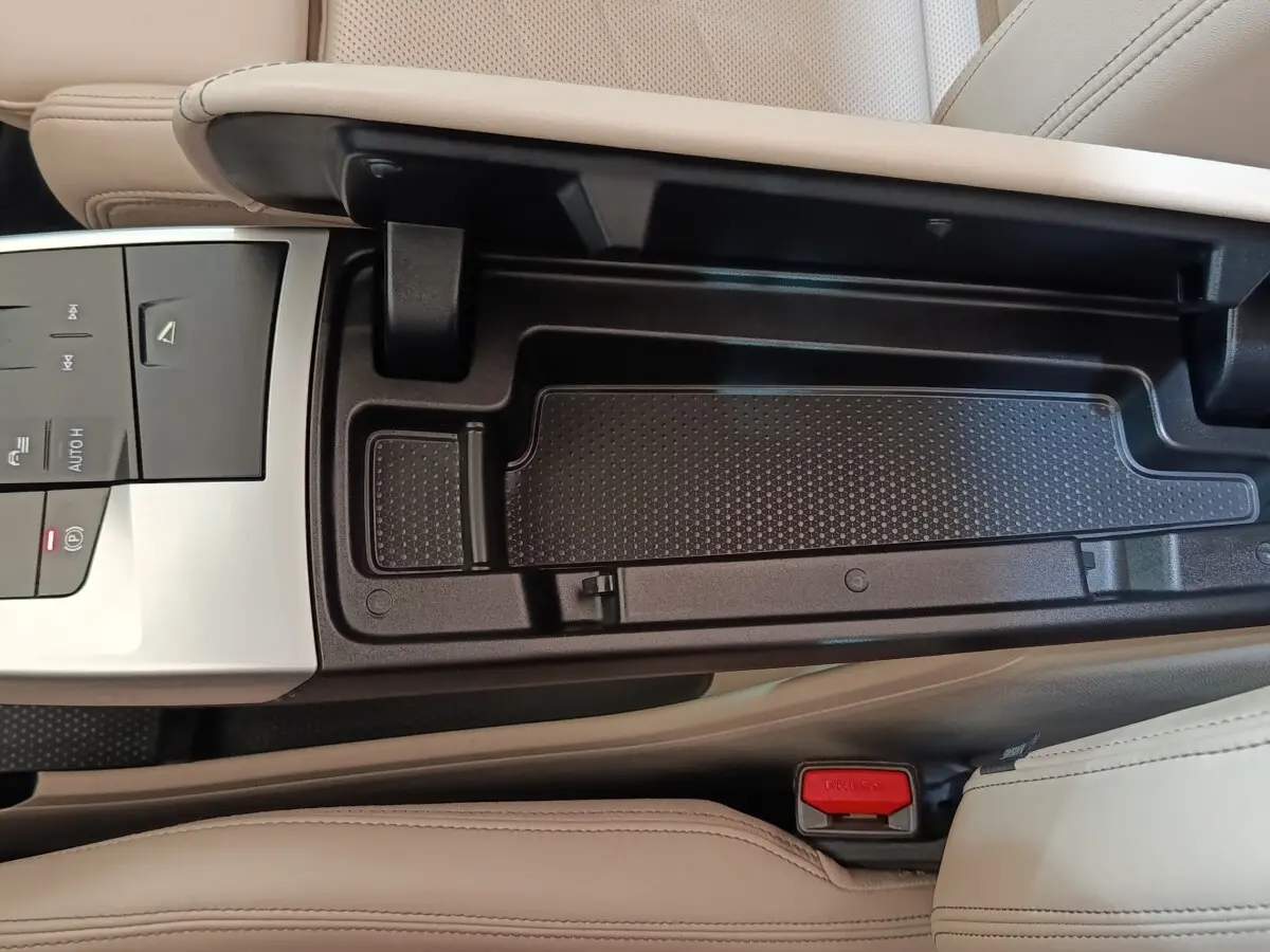 Vue rapprochée de la console centrale beige et noire du BMW X1 xDrive25e M Sport 2024 avec commandes et rangement ouvert.
