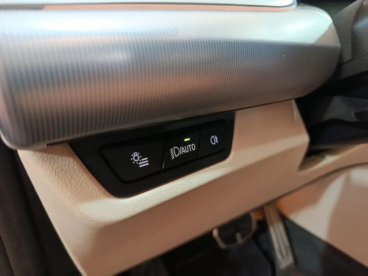 Gros plan sur les commandes d’éclairage automatiques intégrées au tableau de bord beige du BMW X1 xDrive25e M Sport 2024.