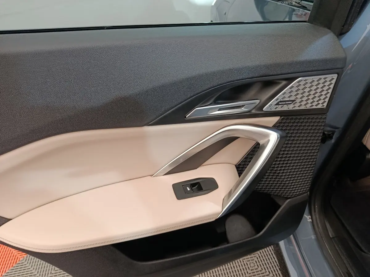 Gros plan sur la porte avant gauche gris foncé du BMW X1 xDrive25e M Sport avec garniture beige et haut-parleur Harman Kardon.