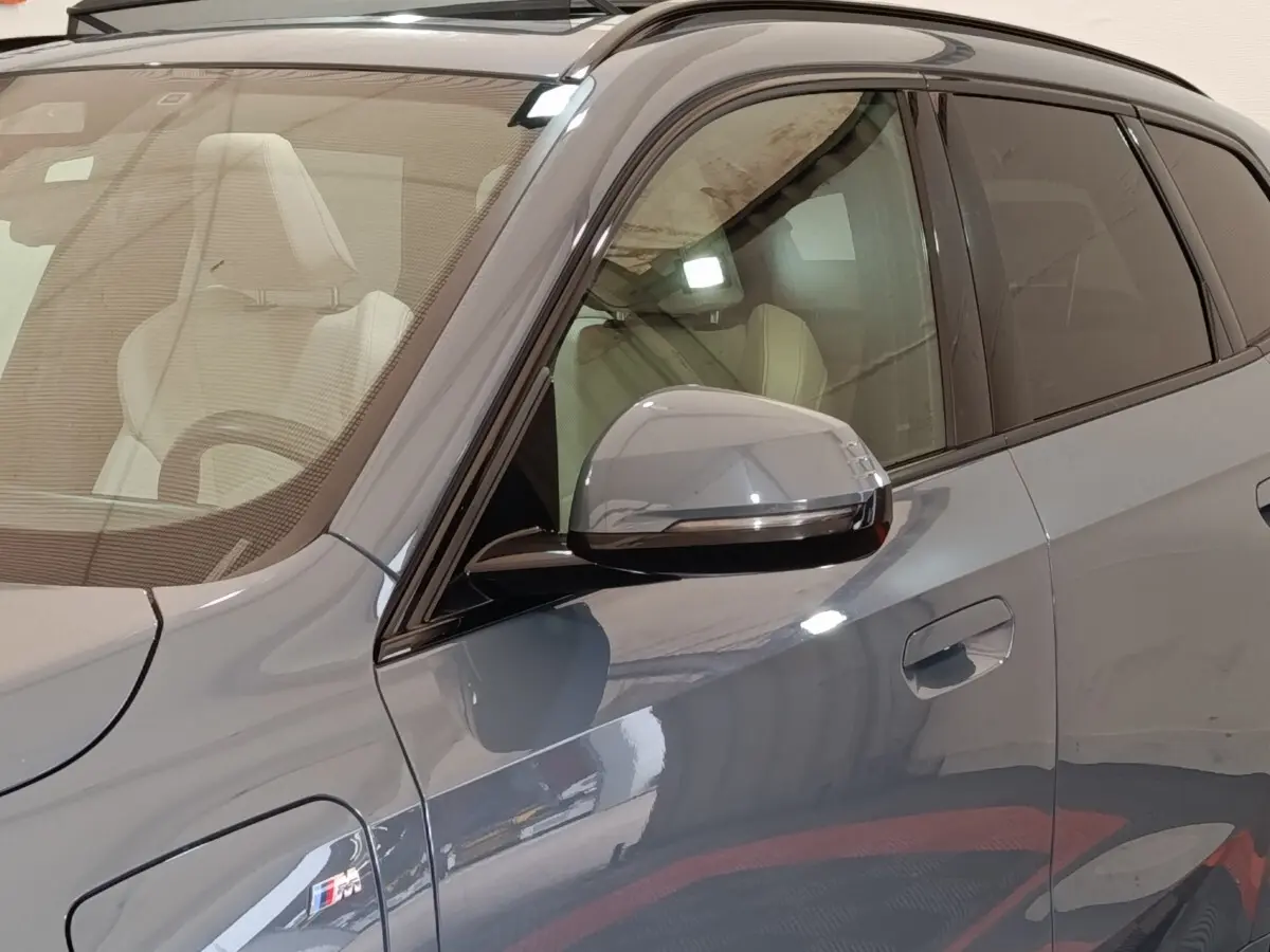 Vue rapprochée côté gauche d’un BMW X1 xDrive25e M Sport gris foncé avec rétroviseur et badge M Sport visibles.