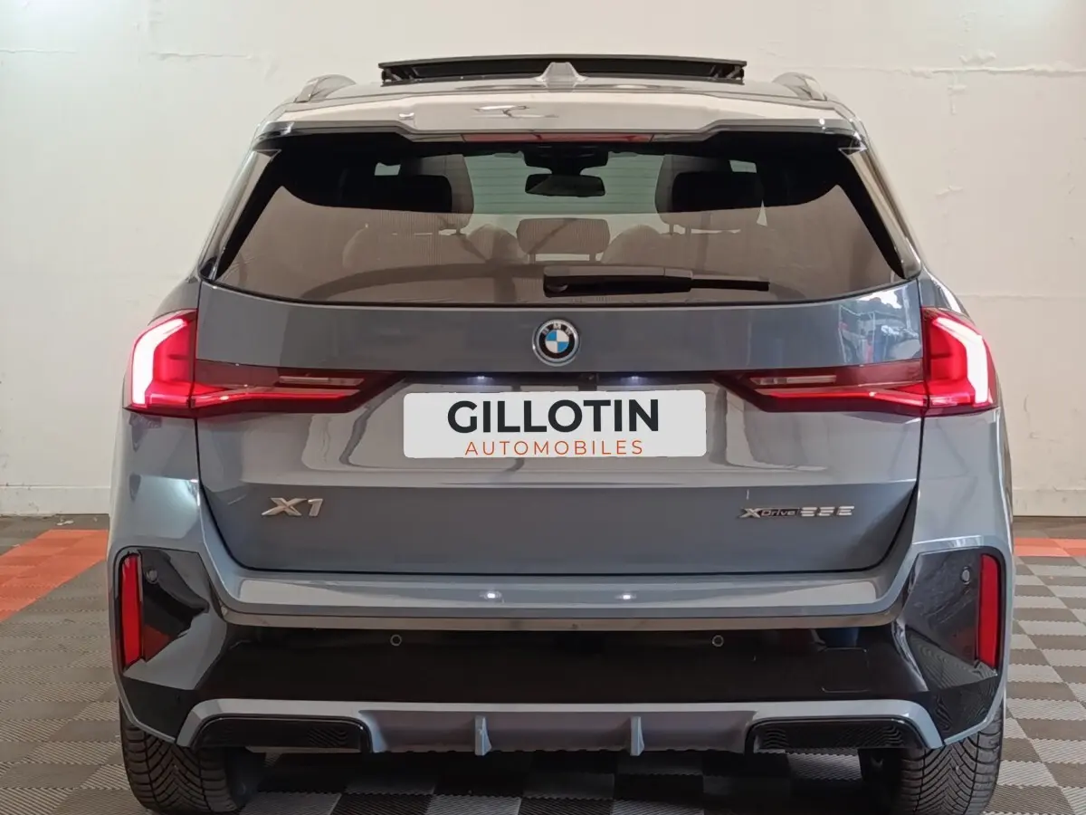 Vue arrière d’un BMW X1 xDrive25e M Sport gris foncé avec feux LED et logo visible sur fond neutre intérieur.