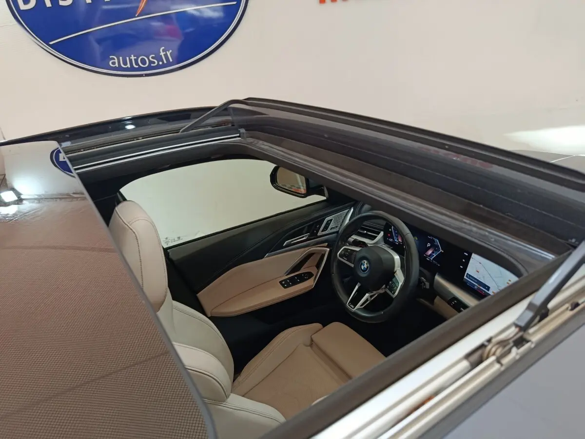 Vue intérieure par le toit ouvrant d'une BMW X1 xDrive25e M Sport 2024 gris foncé, sièges cuir beige et tableau de bord digital.