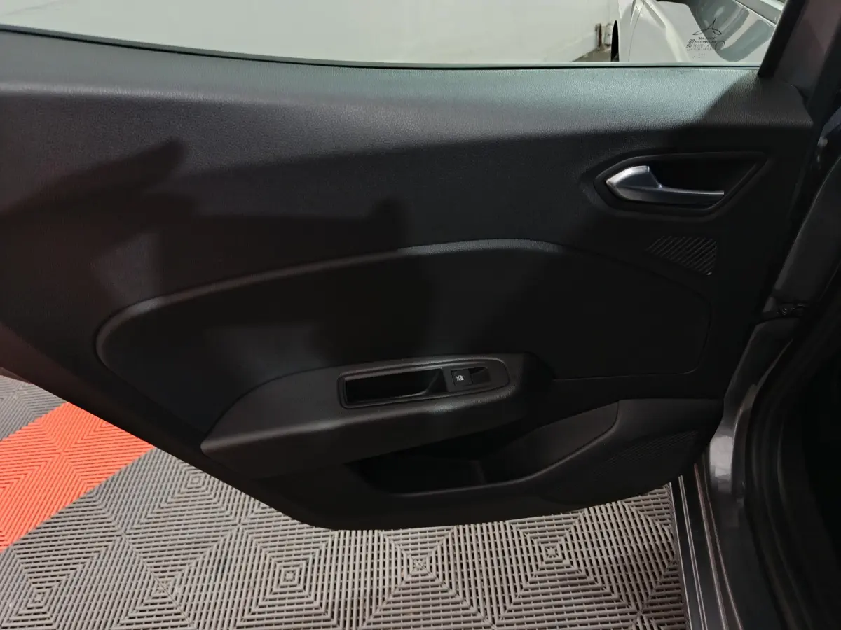 Vue intérieure de la porte côté gauche d'une Renault Clio gris foncé, avec poignée et commande de vitre électrique.