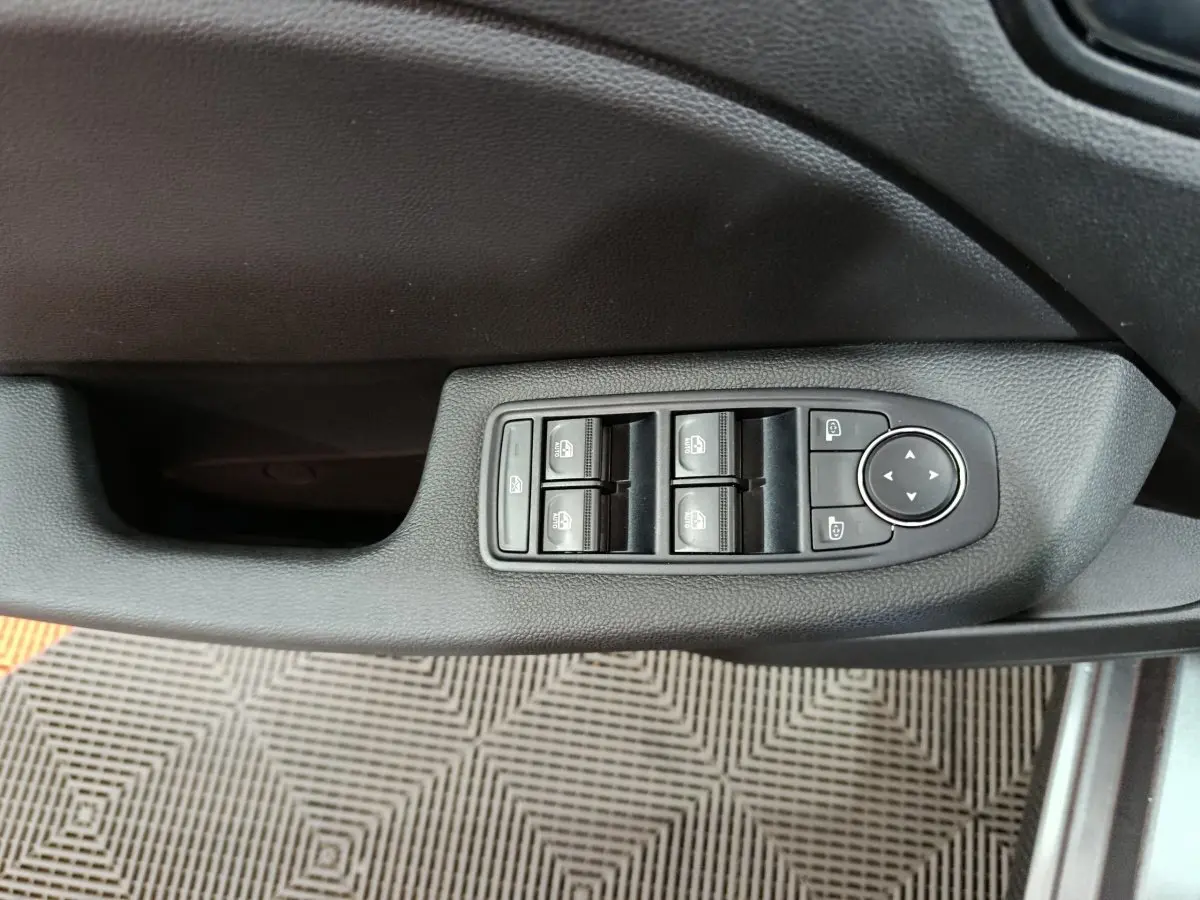 Gros plan sur les commandes des vitres électriques et rétroviseurs côté conducteur d'une Renault Clio gris foncé 2025.