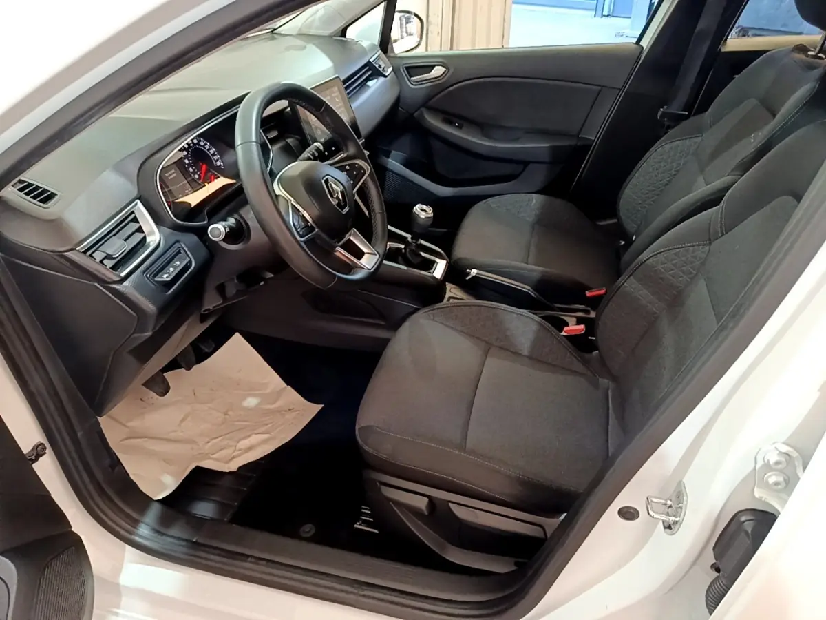 Vue intérieure côté conducteur d'une Renault Clio Business Blue dCi 115 blanche, montrant sièges noirs et volant cuir multifonctions.