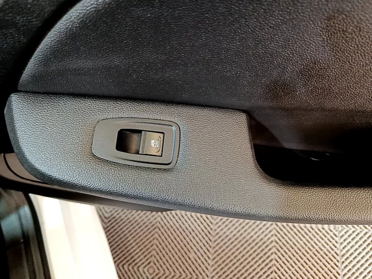 Gros plan sur le bouton de commande de la vitre électrique côté porte arrière d'une Renault Clio blanche.