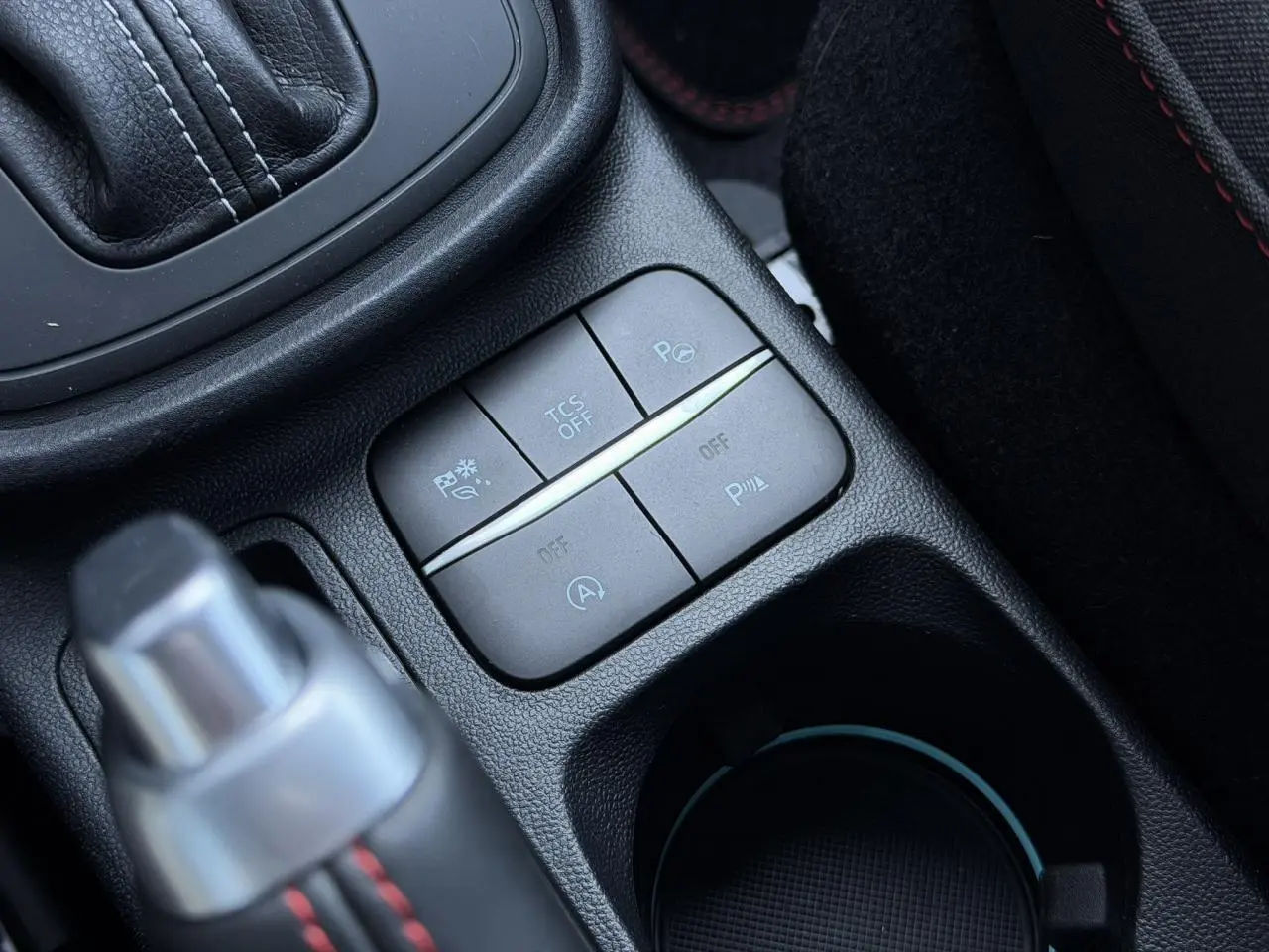 Gros plan sur les commandes du pack sécurité et stationnement dans la console centrale noire du Ford Puma rouge.