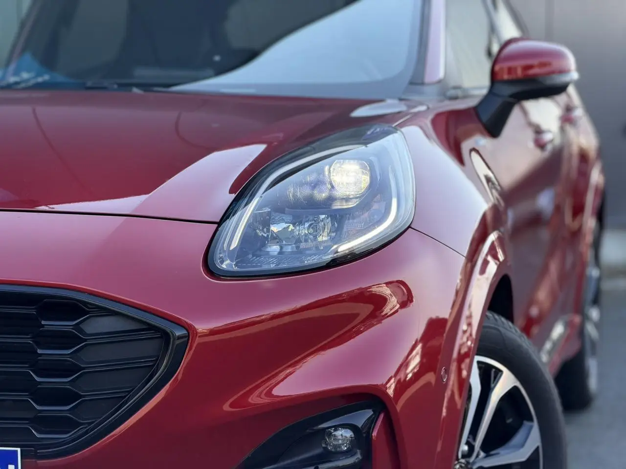 Gros plan sur l’avant droit du Ford Puma rouge Fantastic, mettant en valeur le phare LED et la calandre noire hexagonale.
