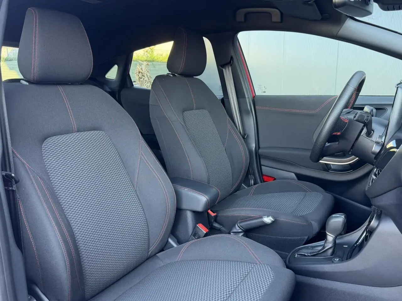 Vue intérieure côté conducteur du Ford Puma rouge, montrant les sièges noirs avec surpiqûres rouges et volant ST-Line.