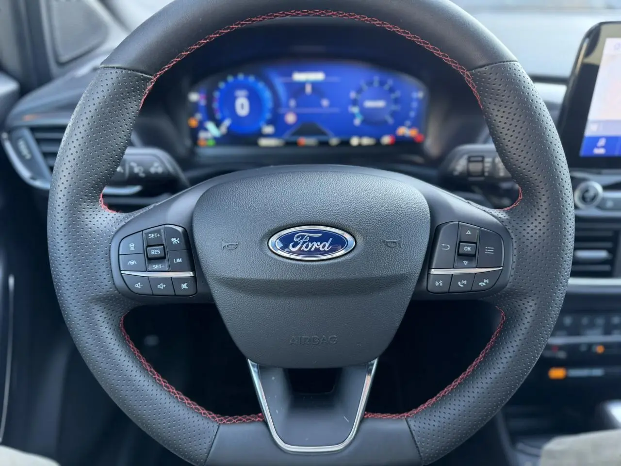 Vue rapprochée du volant perforé noir avec surpiqûres rouges et tableau de bord numérique du Ford Puma 2023.