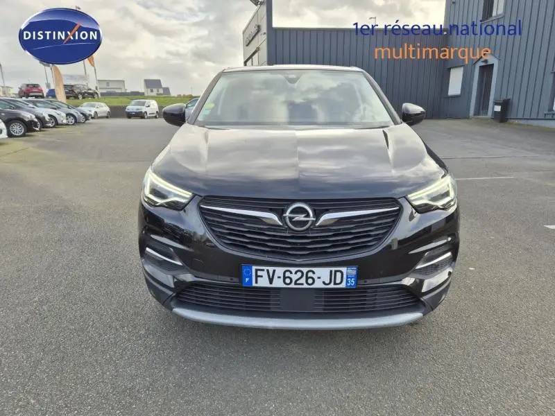 Vue avant d'un Opel Grandland X noir diamant avec calandre chromée et phares LED allumés sur parking extérieur.