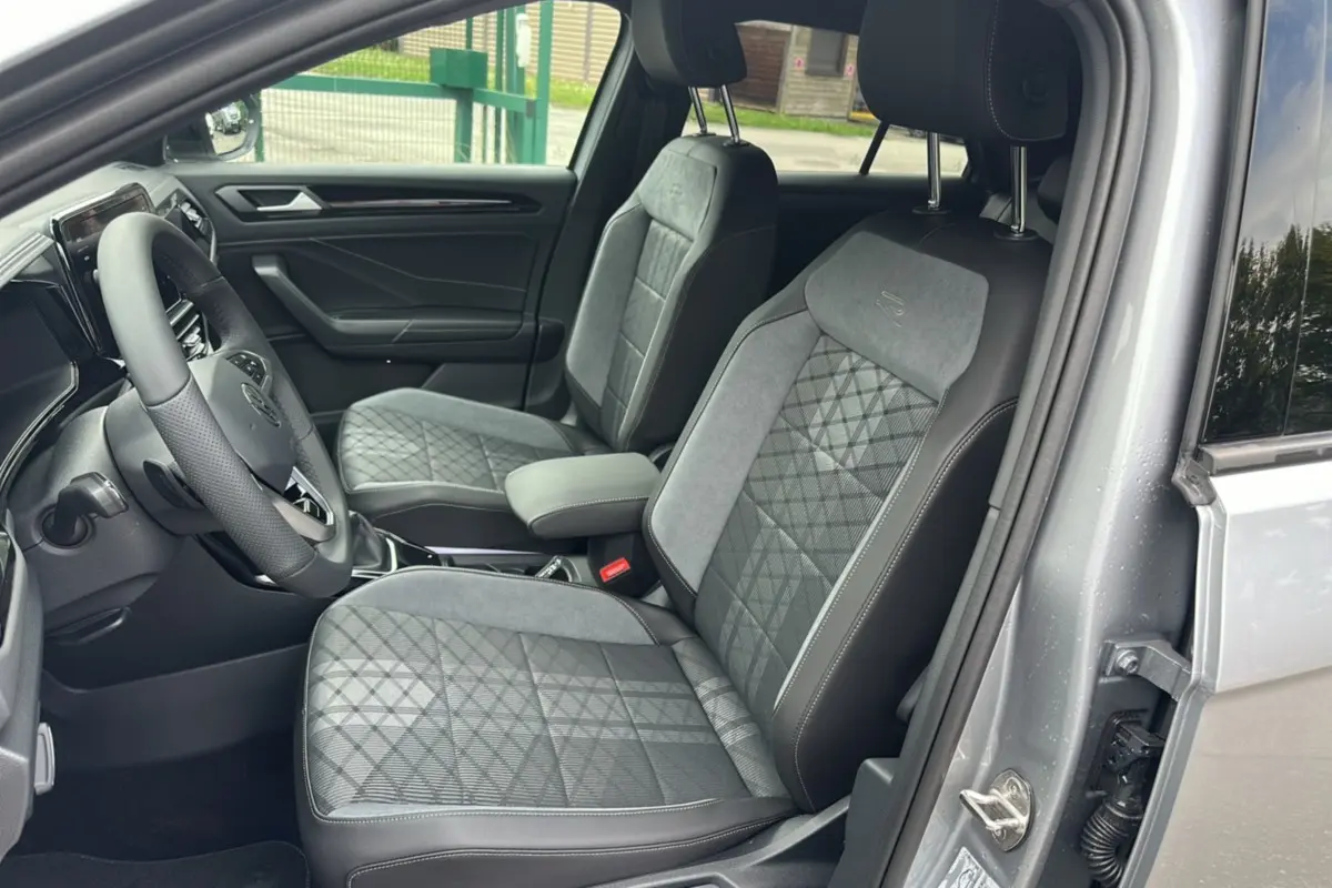 Vue intérieure côté conducteur du Volkswagen T-Roc gris pyrite, mettant en valeur les sièges en tissu avec surpiqûres R-Line.