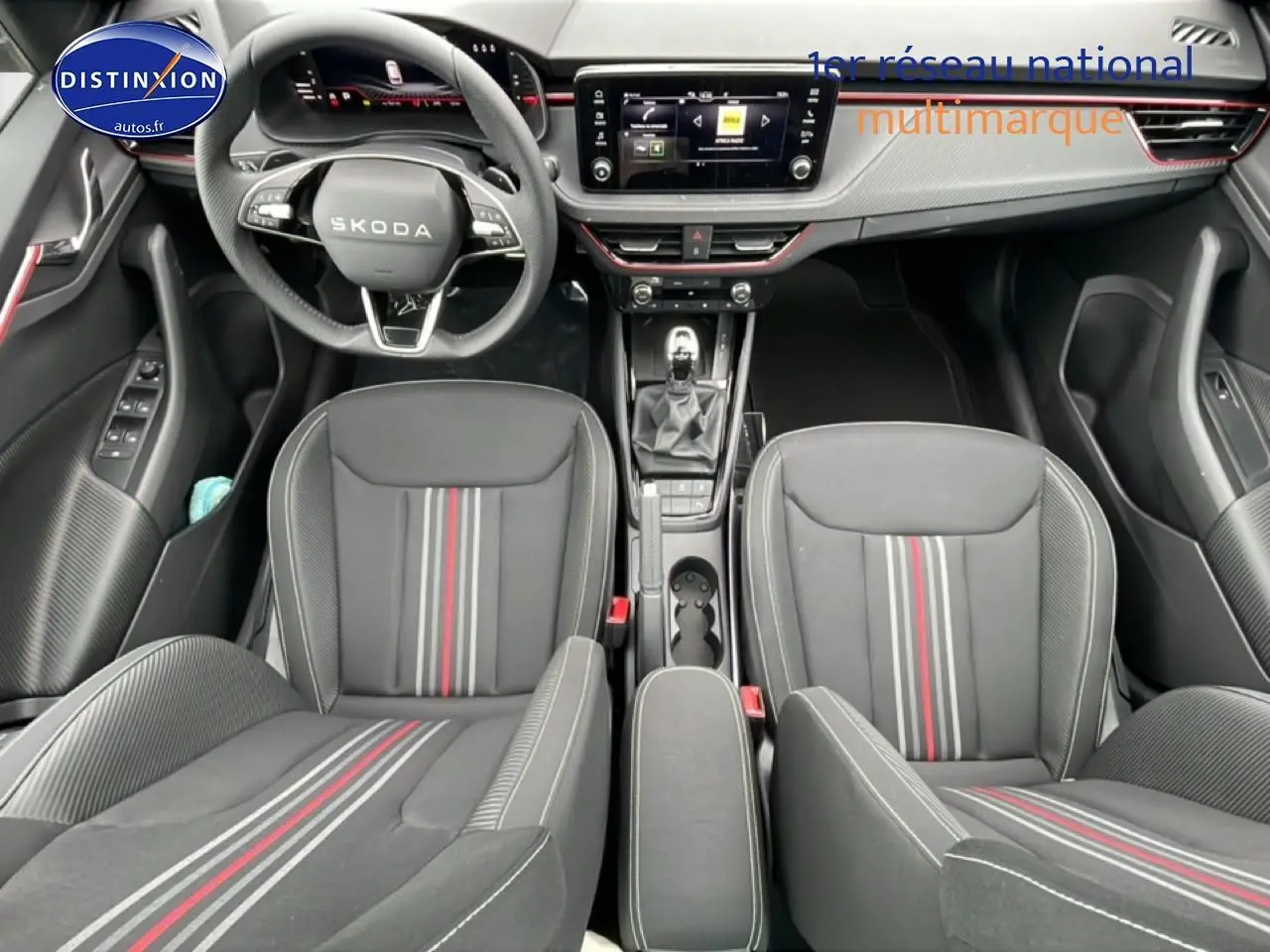 Vue intérieure frontale du Skoda Kamiq noir 2026, mettant en valeur le volant cuir, les sièges sport à bandes rouges et la console centrale.